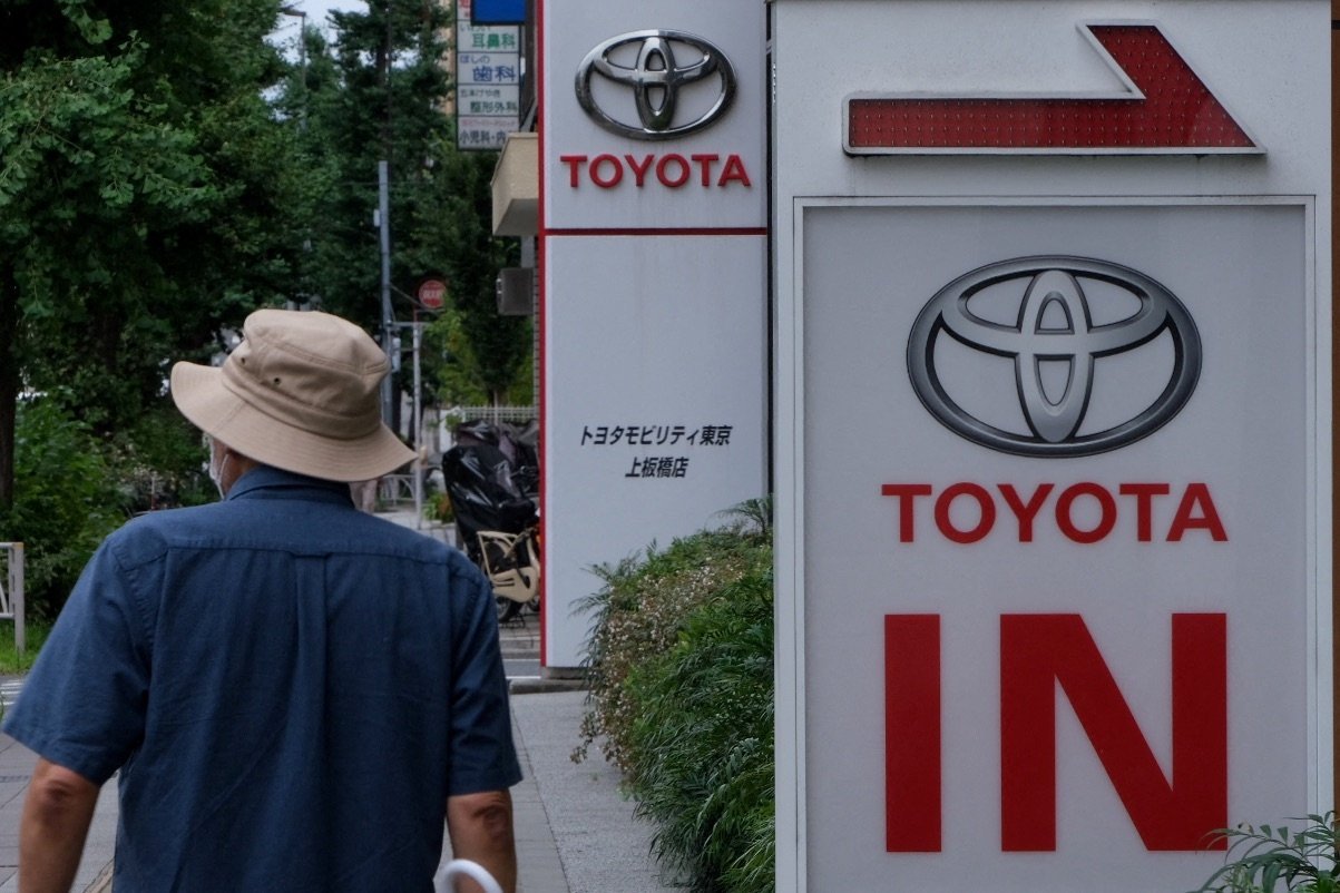 A man walks past signboards for a Toyota Motor car showroom in Tokyo on August 4, 2022. (Photo by Kazuhiro NOGI / AFP)