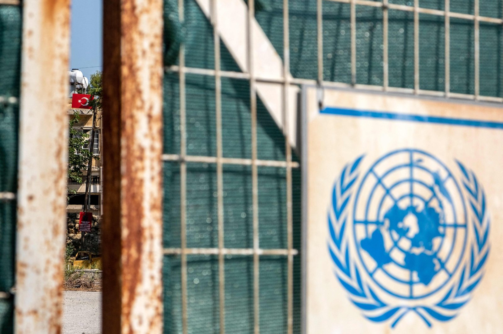 The seal of the United Nations is pictured on a gate leading to the U.N. buffer zone splitting the Cypriot capital Lefkoşa (Nicosia), with a Turkish flag visible in the background in the Turkish Republic of North Cyprus (TRNC), July 11, 2023. (AFP Photo)